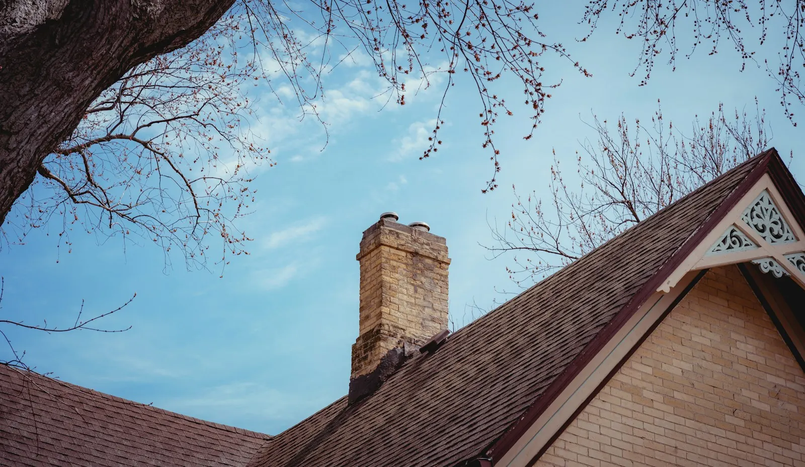 Looking up at a home's roofline and chimney against a blue sky