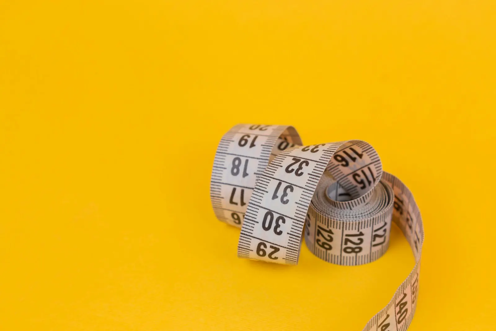Rolled measuring tape on a yellow background