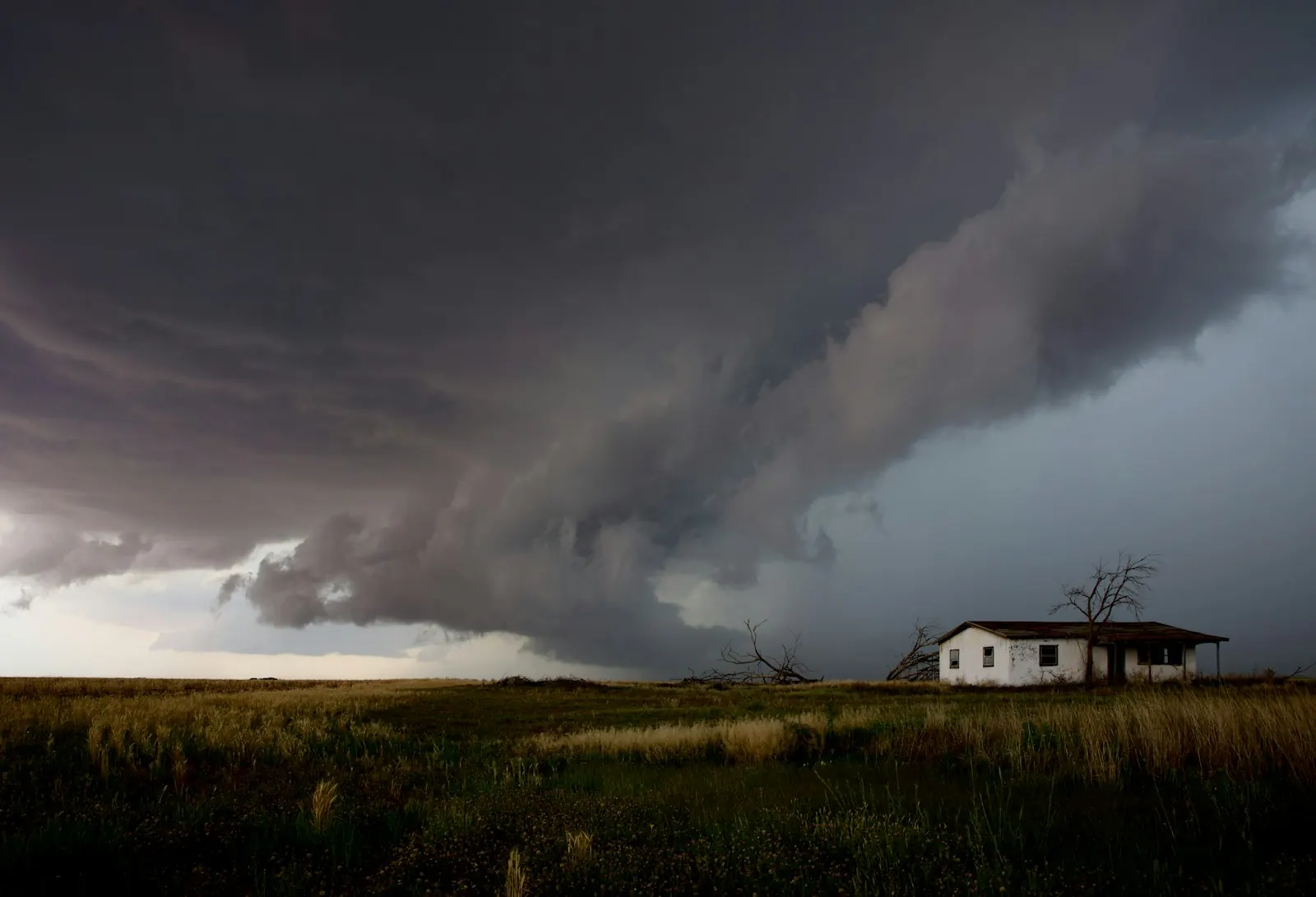 Dark storm clouds approaching a small house in an open field