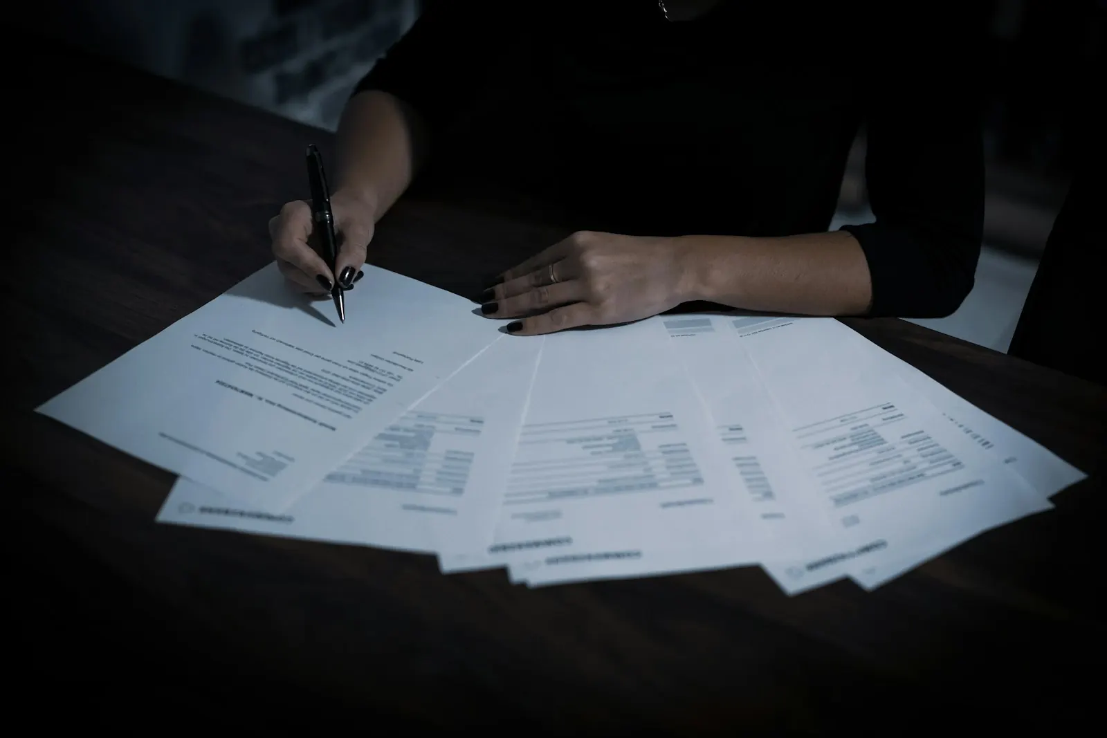 Hands reviewing documents spread across a dark table